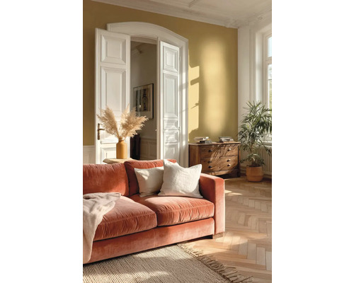 Helles Wohnzimmer mit ockerfarbener Wand, orangefarbenem Samtsofa, Fischgrätparkett, weißen Flügeltüren und Holzkommode.