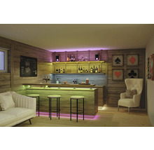 Bar à domicile moderne avec panneaux en bois, comptoir éclairé, tabourets de bar, canapé et fauteuil dans une pièce chaleureuse et organisée.