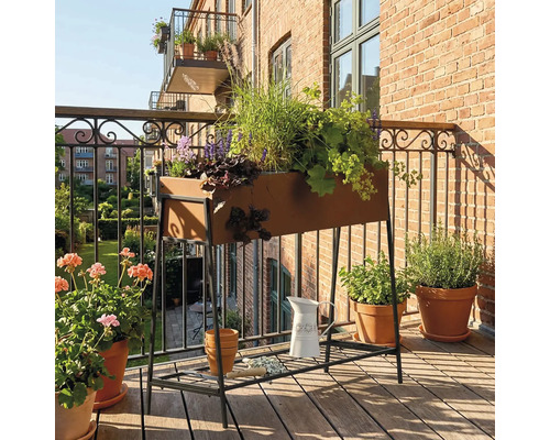 Scène de balcon avec jardinière surélevée plantée, fleurs et arrosoir sur un sol en bois.