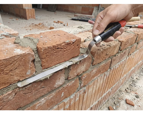 Artisan travaillant un mur de briques avec une truelle à joint