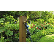Gartenszene mit Wasserhahn, Verteiler und Schlauch an einem Holzpfosten