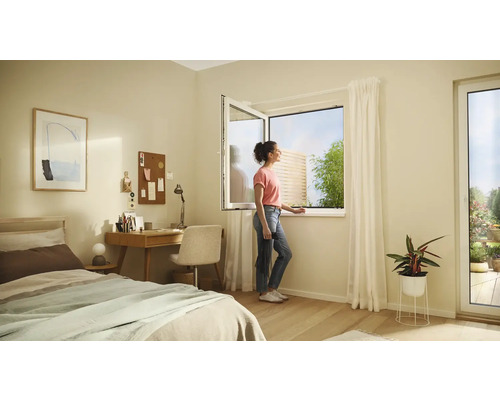 Chambre lumineuse avec un lit, un bureau et une femme ouvrant une fenêtre donnant sur le jardin.