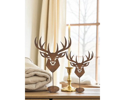 Dekorative Hirschfiguren aus Metall auf einem Tisch, neben einer Kerze und einer gefalteten Decke