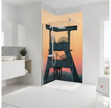 Paroi de douche avec motif industriel d'un chevalement devant un ciel de soirée dans une salle de bains lumineuse.