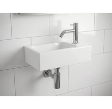 Lavabo en céramique avec robinet et siphon sur un mur carrelé