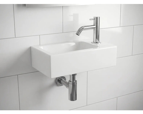 Lavabo en céramique avec robinet et siphon sur un mur carrelé
