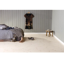 Chambre avec sol clair aspect bois, revêtement mural en panneaux de bois gris, lit avec couvertures et tabouret en bois rustique.