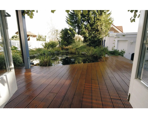 Terrasse en bois faite de planches rainurées avec vue sur un bassin de jardin avec des nénuphars et une végétation luxuriante.