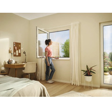 Helles Zimmer mit geöffnetem Fenster, Schreibtisch, Bett und einer Frau, die zum Fenster hinausschaut