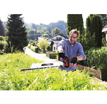 Un homme taille une haie avec un taille-haie dans un jardin.