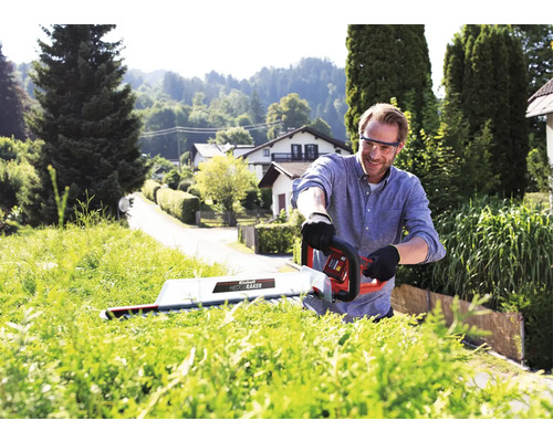 Un homme taille une haie avec un taille-haie dans un jardin.