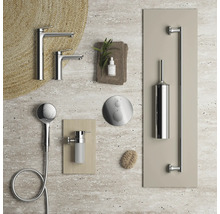 Anordnung moderner verchromter Badezimmerarmaturen wie Waschtischmischer, Handbrause, Duschsteuerung, Seifenspender und Toilettenbürstenhalter auf Stein