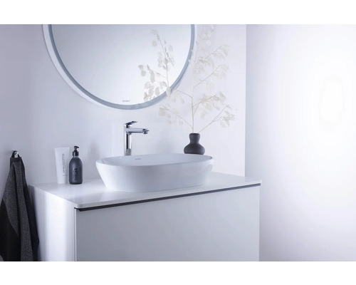 Modernes Badezimmer mit weißem Aufsatzwaschbecken auf einem weißen Waschtischunterschrank, verchromter Armatur und rundem Wandspiegel.