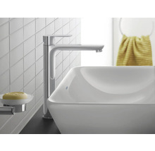 Moderne, hohe Waschtischarmatur in Chrom an einem weißen Aufsatzwaschbecken in einem hellen Badezimmer mit weißen Fliesen.