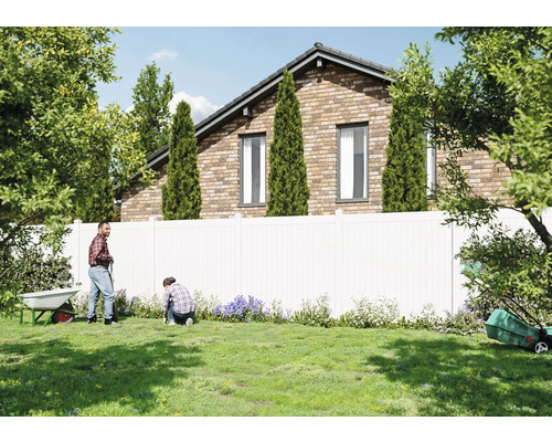 Gartenszene mit Personen, Rasen, Zaun und Haus im Hintergrund