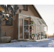 Wäisst Anlehn-Gewächshaus mat Glaswänn un engem Haus am Schnéi. Eng Persoun liest am hellen, ageriichten Innenraum.