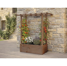 Jardinière en bois avec treillis intégré et pergola, plantée de fleurs et de tomates devant un mur en pierre naturelle.