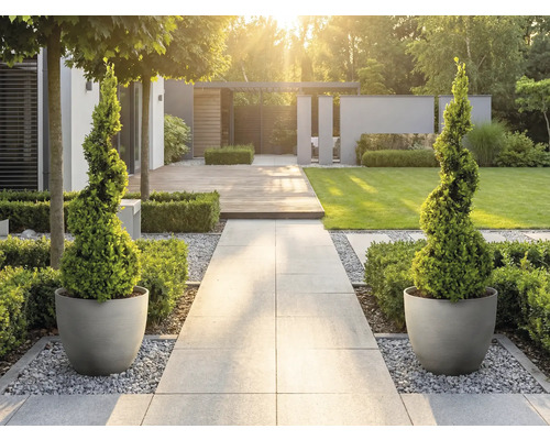 Jardin moderne et lumineux avec chemin en pierre, buis taillés en spirale dans des pots ronds, terrasse en bois et pelouse.