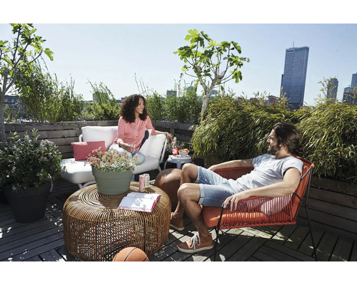 Terrasse de toit relaxante avec mobilier de salon, une table en rotin et des plantes en pot devant une ligne d'horizon urbaine.