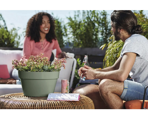 Deux personnes assises sur une terrasse autour d une table ronde en rotin avec un pot de fleurs vert clair contenant des succulentes.