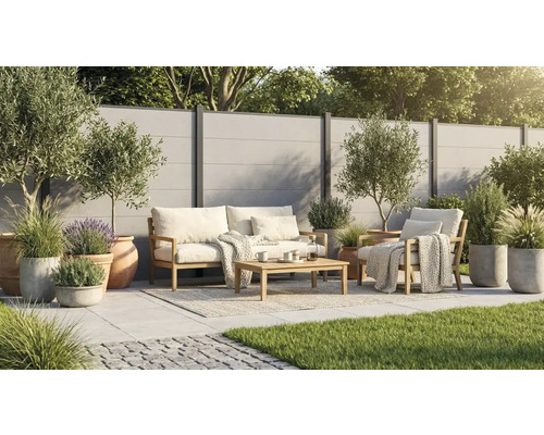 Salon de jardin moderne en bois sur une terrasse carrelée claire avec clôture, oliviers et graminées en pots.