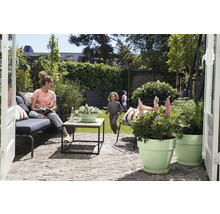 Terrasse moderne avec pavés, meubles de jardin, table basse et pots de fleurs avec des enfants qui jouent sur la pelouse à l arrière-plan.