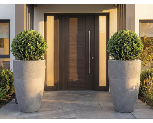 Porte d'entrée moderne aspect bois avec longue poignée métallique, flanquée de deux parois latérales mates et de grands pots de fleurs gris.