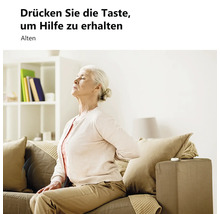 Ältere Frau mit Rückenschmerzen auf einem Sofa im hellen Wohnzimmer, neben einem Notfallknopf auf der Armlehne.