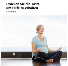 Eine schwangere Frau meditiert auf dem Boden neben einem an der Fußleiste montierten Notrufknopf mit dem Text Drücken Sie die Taste um Hilfe zu erhalten.