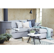 Modernes Wohnzimmer mit grauem Ecksofa, Zierkissen, hellblauer Wohndecke, weißem Beistelltisch mit Pflanzen und einem grauen Kaminofen.