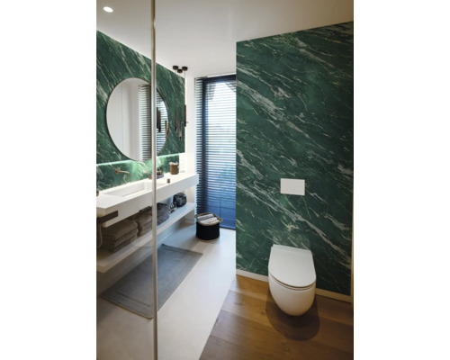 Salle de bains moderne avec murs aspect marbre vert, lavabo blanc, miroir rond et WC suspendu.