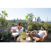 Toit-terrasse lumineux avec vue urbaine, mobilier de jardin, plantes en pot et deux personnes sur un platelage en bois.
