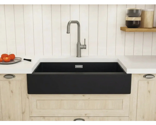 Schwarze Schürzen-Spüle in einer hellen Holzküche mit einer hohen gebürsteten Armatur und weißer Arbeitsplatte.