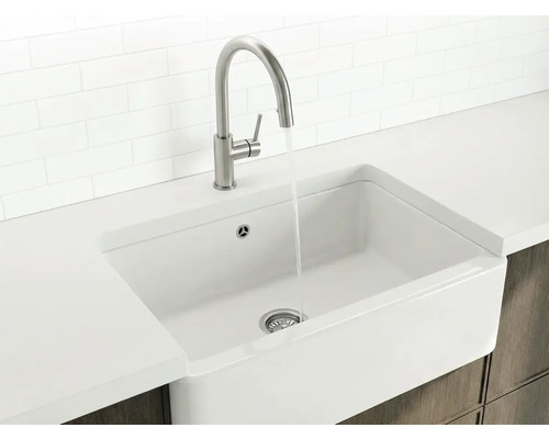 Weißes Spülbecken im Landhausstil mit hohem Wasserhahn aus Metall und fließendem Wasser in einer hellen, organisierten Küche.