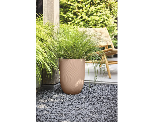 Grand pot de fleurs rond avec une texture ondulée et des graminées ornementales sur du gravier dans un jardin avec une chaise en bois.