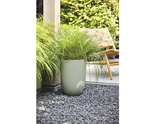 Grand pot de fleurs vert clair avec structure ondulée et herbe ornementale sur gravier gris dans le jardin.