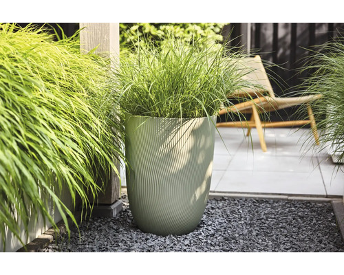 Grand pot de fleurs moderne avec structure ondulée verticale et graminées sur une terrasse lumineuse et organisée avec gravier et dalles.