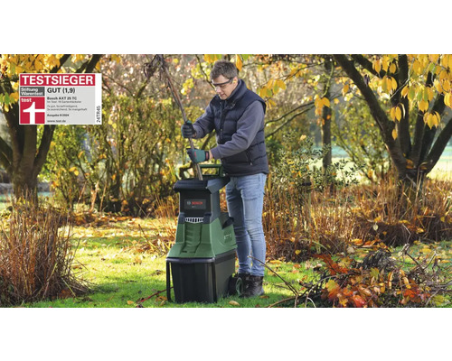 Homme utilisant le broyeur Bosch AXT 25 TC au jardin avec lunettes et gants. Sceau du vainqueur du test Stiftung Warentest.