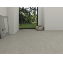 Pièce moderne et lumineuse avec sol en vinyle gris clair aspect béton, grande fenêtre donnant sur le jardin et un pouf.