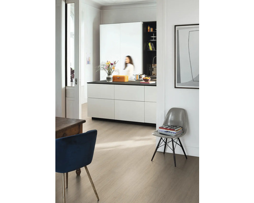 Pièce moderne et lumineuse avec un sol stratifié aspect bois clair, un îlot de cuisine blanc avec plan de travail noir et des chaises design.