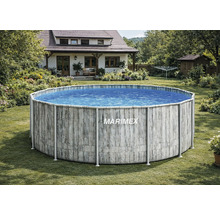 Une piscine hors sol ronde Marimex avec un décor en bois gris dans un jardin verdoyant devant une maison individuelle.
