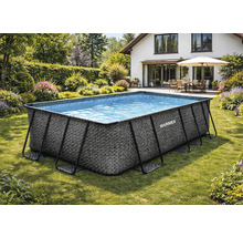 Rechteckiger Marimex Frame Pool mit Rattan-Optik auf einer Rasenfläche in einem Garten mit Blumen und Hecken.