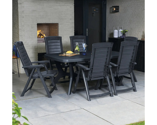 Salon de jardin en plastique foncé avec table rectangulaire et chaises à dossier haut sur une terrasse avec cheminée et sol carrelé.