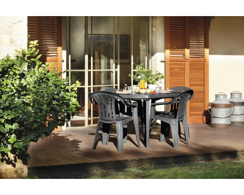 Set de mobilier de jardin en plastique avec table ovale et fauteuils sur une terrasse en bois ensoleillée devant la maison.