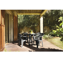 Salon de jardin avec table ronde noire et quatre fauteuils en plastique sur une terrasse en bois ensoleillée sous une pergola.