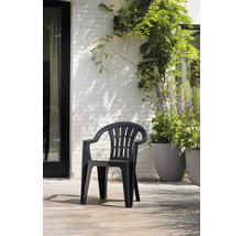 Chaise de jardin empilable en plastique noir avec accoudoirs sur une terrasse claire devant un mur en briques blanches avec des plantes.