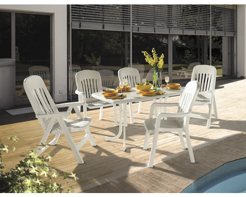 Salon de jardin composé d une table et de cinq chaises en plastique blanc sur une terrasse en bois à côté d une piscine.