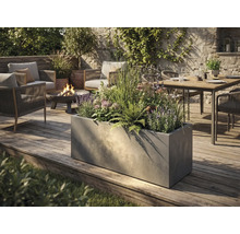 Grand bac à plantes rectangulaire aspect béton sur une terrasse en bois dans un jardin moderne avec salon de jardin et brasero.