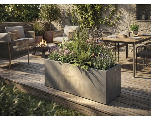 Grand bac à plantes rectangulaire aspect béton sur une terrasse en bois dans un jardin moderne avec salon de jardin et brasero.
