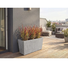 Jardinière rectangulaire grise aspect pierre avec herbe ornementale sur une terrasse de toit avec plancher en bois et meubles de salon.